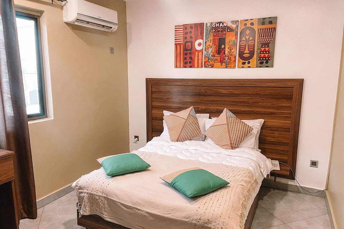 Una cama bien hecha con cabecera de madera, dos almohadas verdes y una colcha color beige.