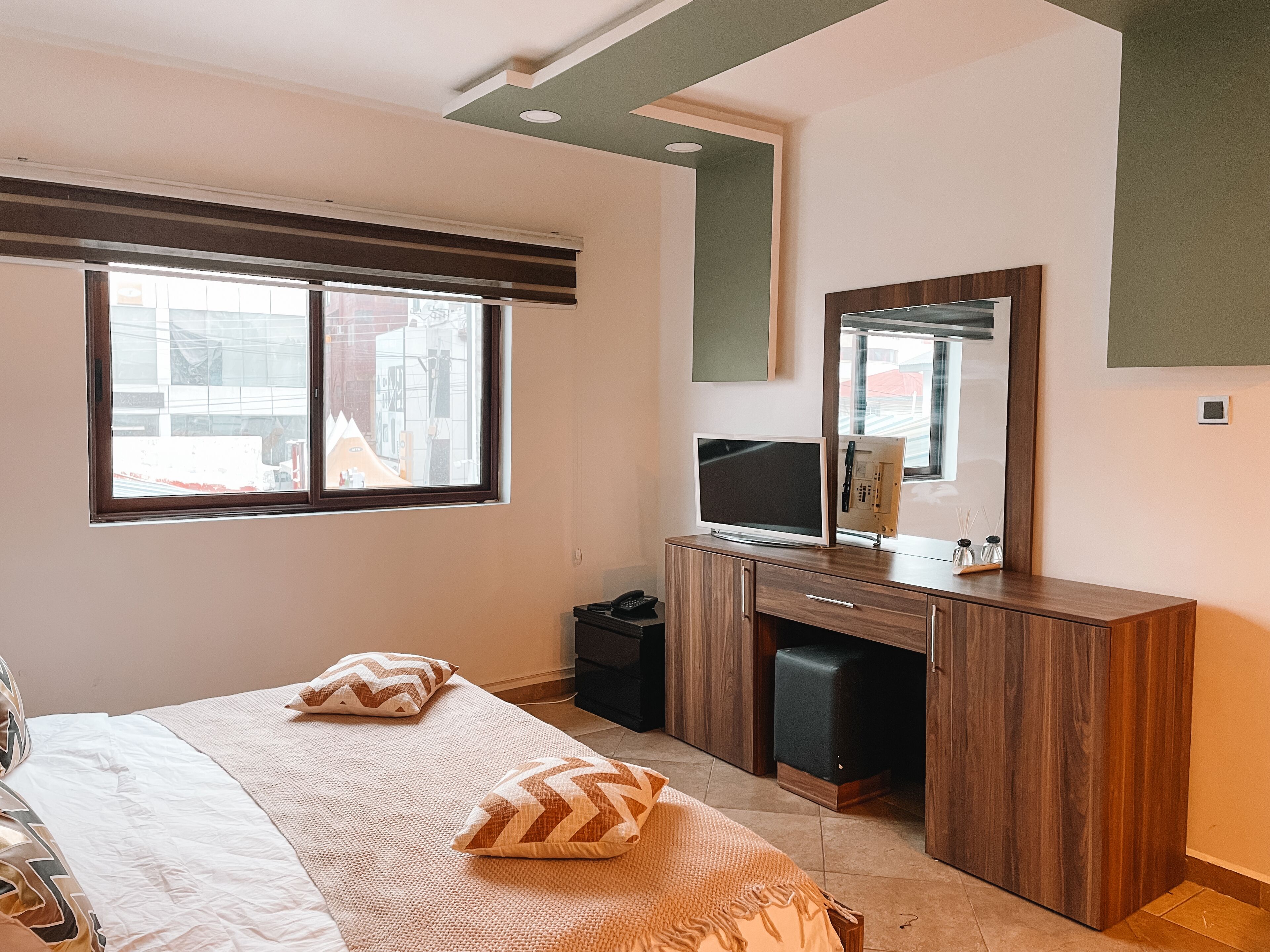 Ein Schlafzimmer mit einem Bett, zwei Kissen, einem Schminktisch, einem Fernseher und einem Spiegel.