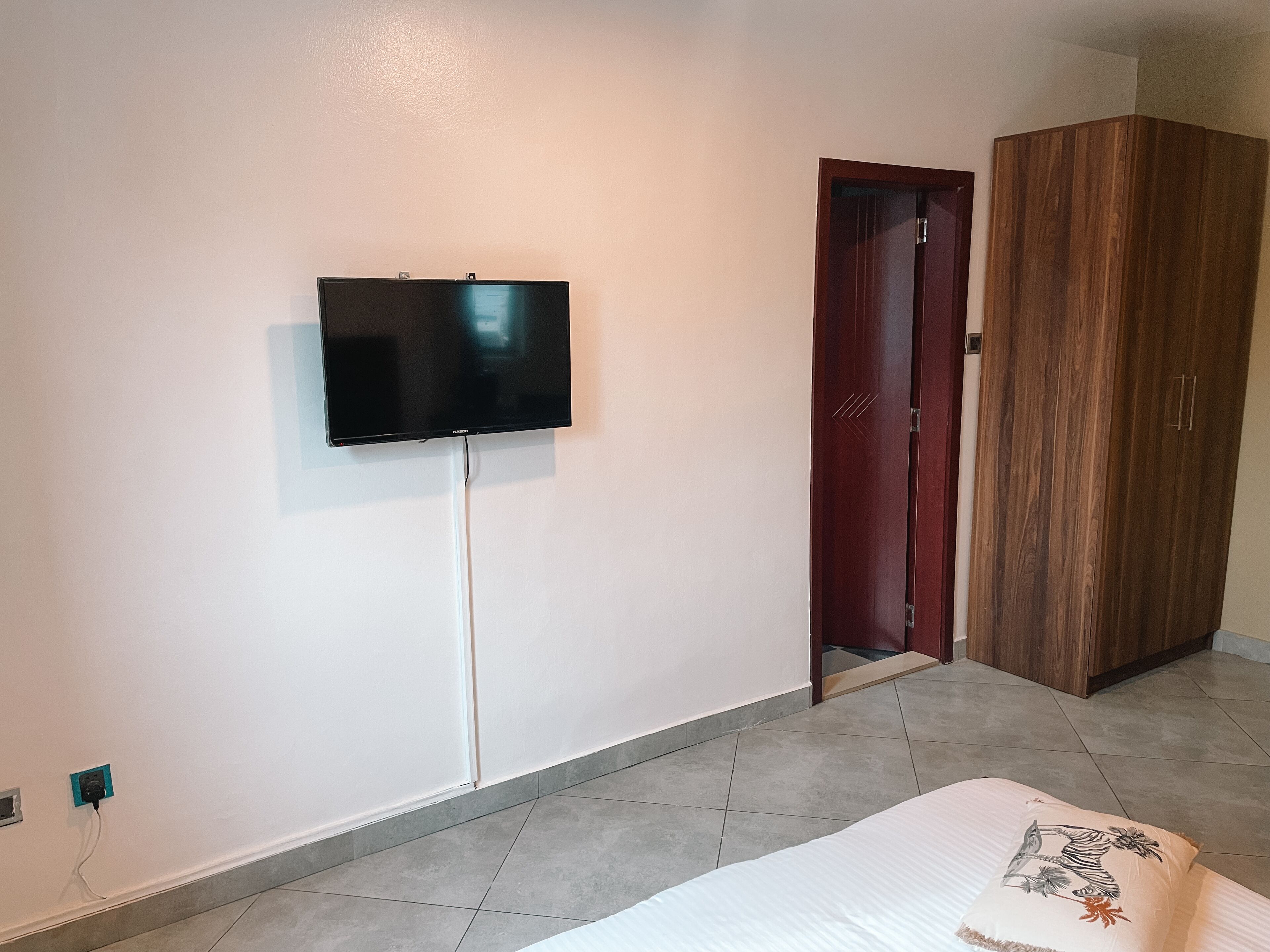 A bedroom with a bed, a television mounted on the wall, a wardrobe, and a door.