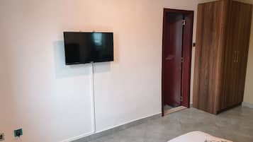 A bedroom with a bed, a television mounted on the wall, a wardrobe, and a door.