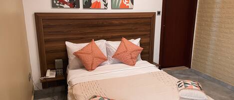 A neatly made bed with patterned pillows, a wooden headboard, and a wall with three artworks.