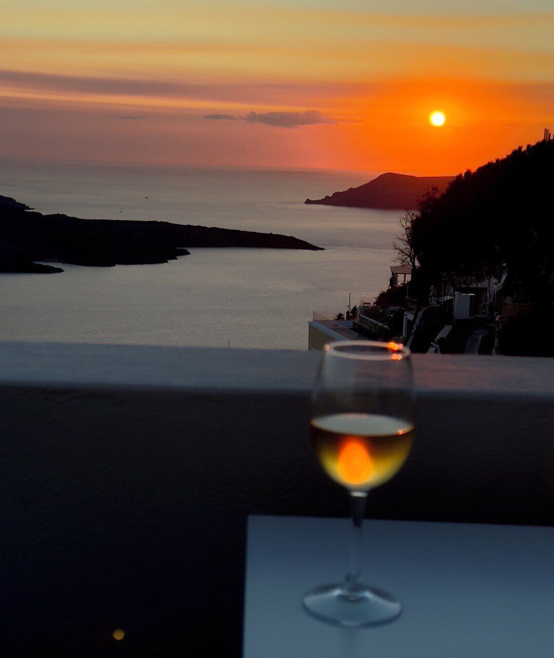A sunset view from a balcony with a glass of wine.