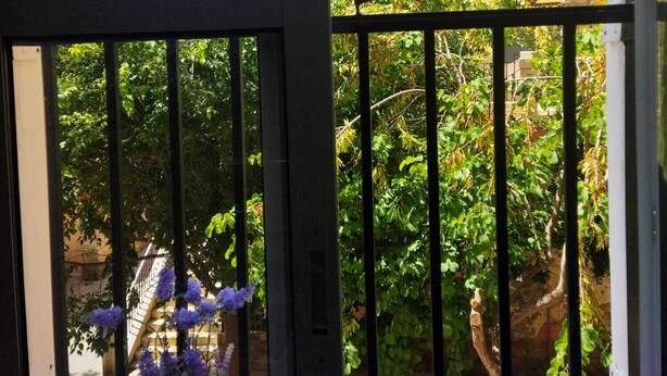 Une entrée fermée par un portail, d’où l’on aperçoit un jardin et un bâtiment en arrière-plan.