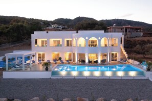 A modern two-story house with a swimming pool, outdoor seating, and a view of the surrounding hills.