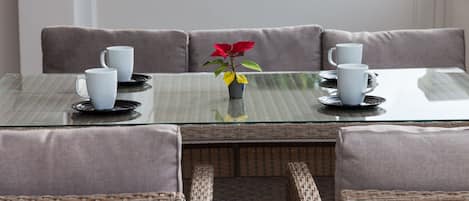 A dining table with four white cups and saucers, a vase with a red flower, and wicker chairs.