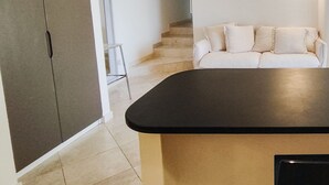 Moderni keittiö, jossa on musta työtaso, valkoinen sohva ja portaat, jotka johtavat toiseen huoneeseen.