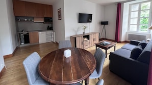 A modern living room with a wooden dining table, grey sofa, and a flat-screen TV mounted on the wall. - Résidence thermale de la Chaldette (Brion)