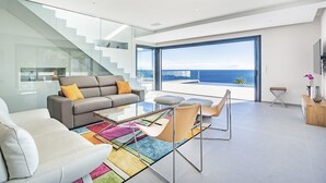 Ein modernes Wohnzimmer mit einer Glaskonstruktion als Treppe, einem Sofa, einem Couchtisch und Blick auf den Ozean.