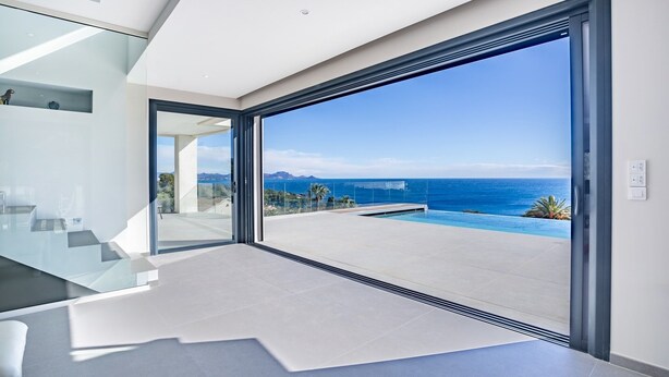 Ein modernes Interieur mit einer großen Glasdoor, die auf einen Balkon mit Pool und Meerblick führt.