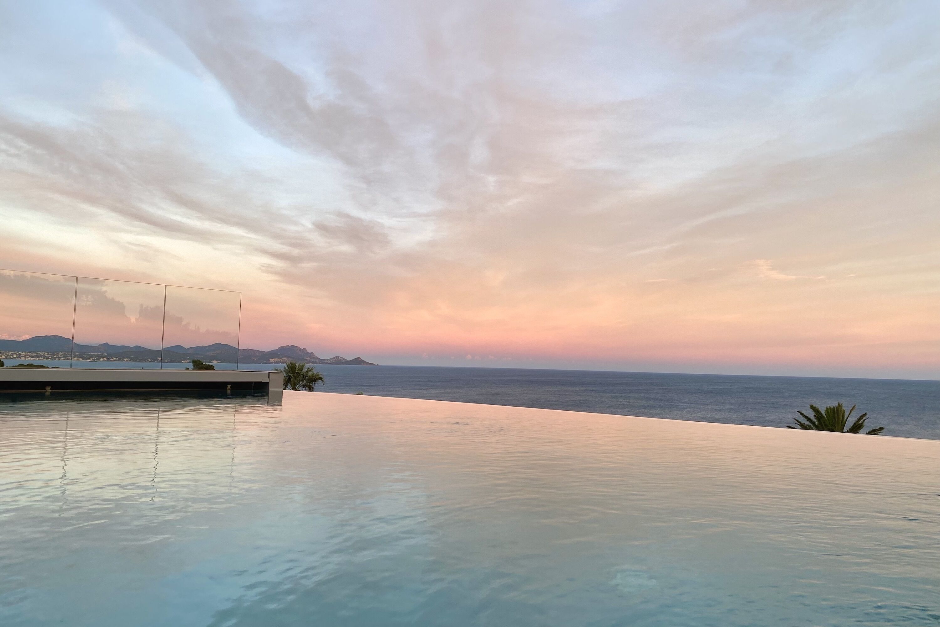 Une piscine à débordement offrant une vue sur l’océan et les montagnes au coucher du soleil.