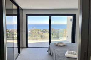 Ein Schlafzimmer mit einer großen Schiebeglastür, die auf einen Balkon mit Blick auf das Meer und die umliegende Landschaft führt.