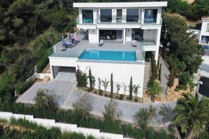 Ein modernes, zweistöckiges Haus mit Swimmingpool, Sitzgelegenheit im Freien und einem gepflegten Garten.