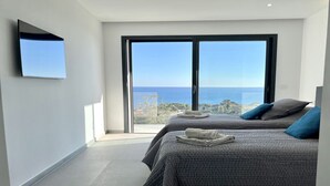 Ein Schlafzimmer mit zwei Betten, einem großen Fenster mit Meerblick und einem an der Wand montierten Flachbildfernseher.