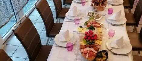 Una larga mesa de comedor servida con platos, vasos y diversos platillos, rodeada de sillas en una habitación con ventanas amplias.