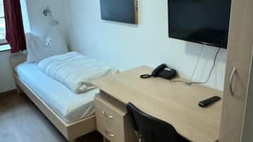 Una habitación pequeña y ordenada con cama, escritorio, silla, televisión y ventana con cortinas.