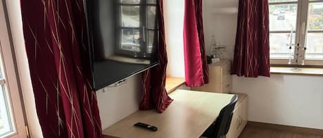 A room with a bed, a desk, a TV, and a window with curtains.