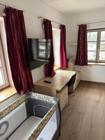 Una habitación con cama, escritorio, televisor y ventana con cortinas.
