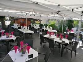 Un restaurante al aire libre con mesas dispuestas bajo toldos blancos, cada una con servilletas rosas y un pequeño arreglo floral.
