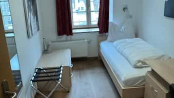 A small, clean room with a bed, a bedside table, a radiator, a window with curtains, and a wall-mounted picture.