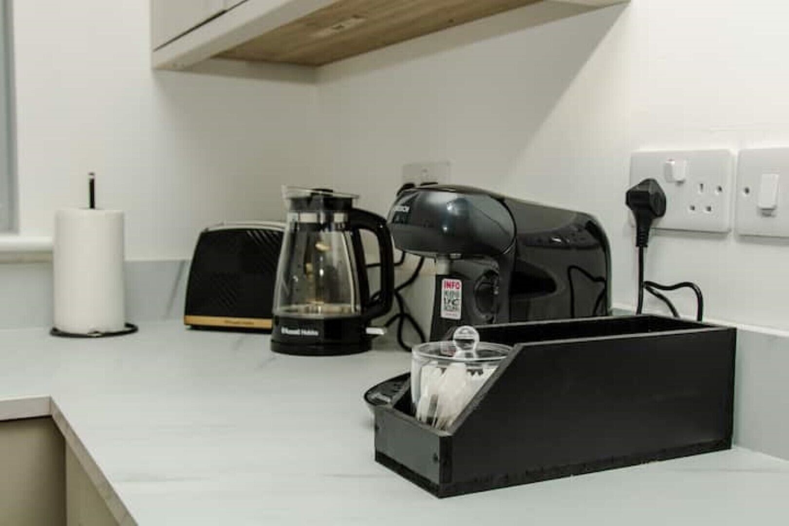 A kitchen with a coffee maker, toaster, and a black container with utensils.