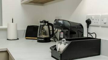 A kitchen with a coffee maker, toaster, and a black container with utensils.