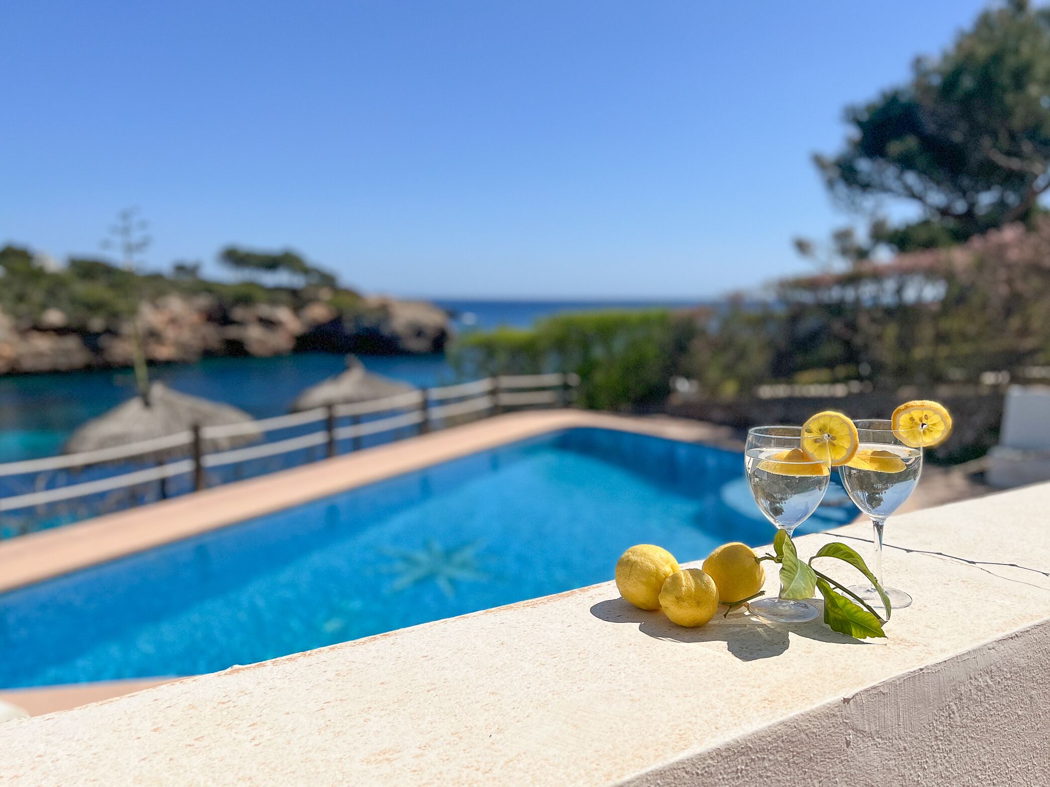 A poolside view with a clear blue pool, a wooden deck, and a glass of water with lemon slices.