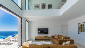 A modern living room with a large sofa, a TV, and a view of the ocean. - Villa La Grande Bleue met Verwarmd Privé Zwembad (AN)