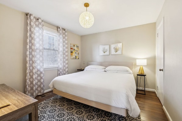 A bedroom with a bed, a bedside table, a lamp, a window with curtains, and a ceiling light.
