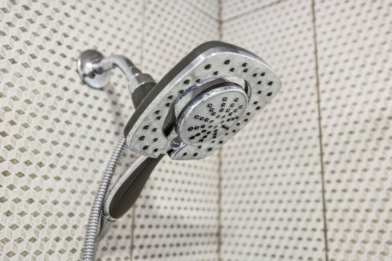 Un cabezal de ducha con diseño perforado, sujeto a una pared con azulejos de diseño de rombos.