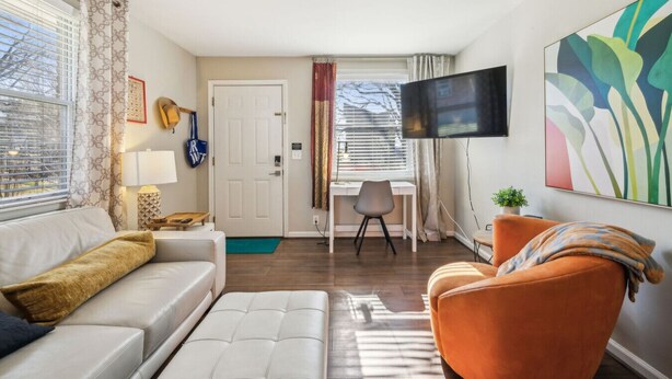 Ein modernes Wohnzimmer mit einem weißen Sofa, einem orangefarbenen Sessel und einem an der Wand montierten Fernseher.