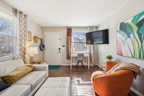 Un salon moderne avec un canapé blanc, un fauteuil orange et un téléviseur fixé au mur.