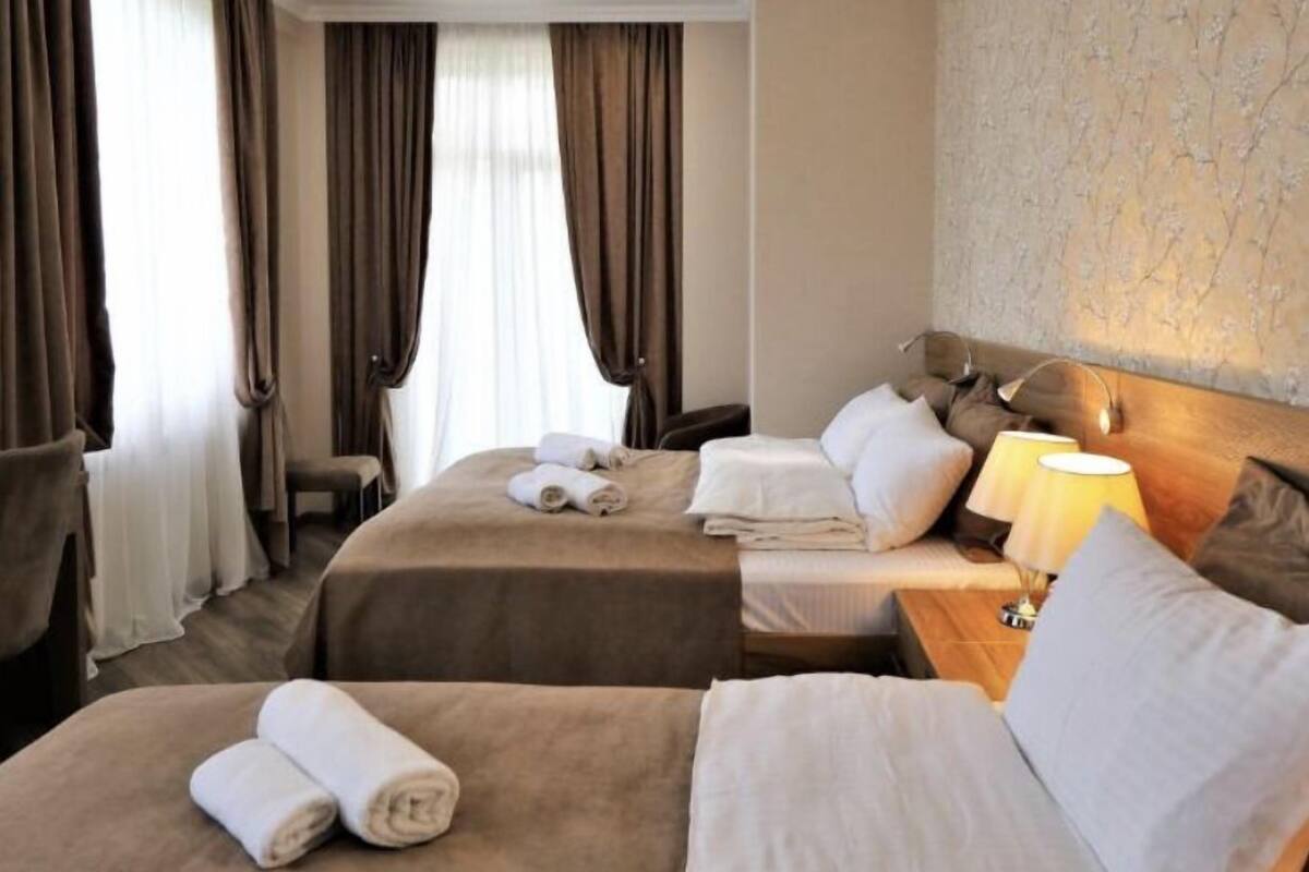 A hotel room with two beds, a desk, a chair, and a lamp.