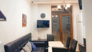 A modern living room with a sofa, dining table, chairs, a flat-screen TV, and a clock on the wall.