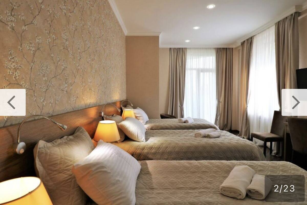 A hotel room with two beds, a headboard, lamps, a TV, and curtains.