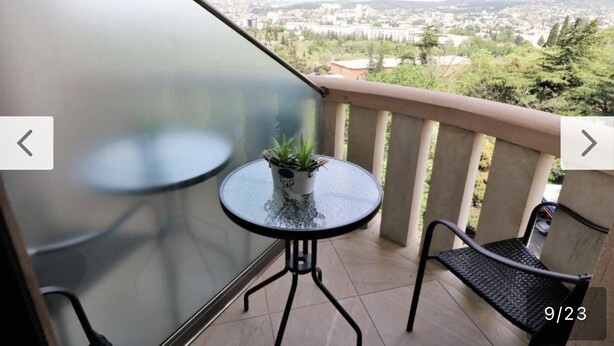 A balcony with a glass table and chairs, a potted plant, and a view of a cityscape.