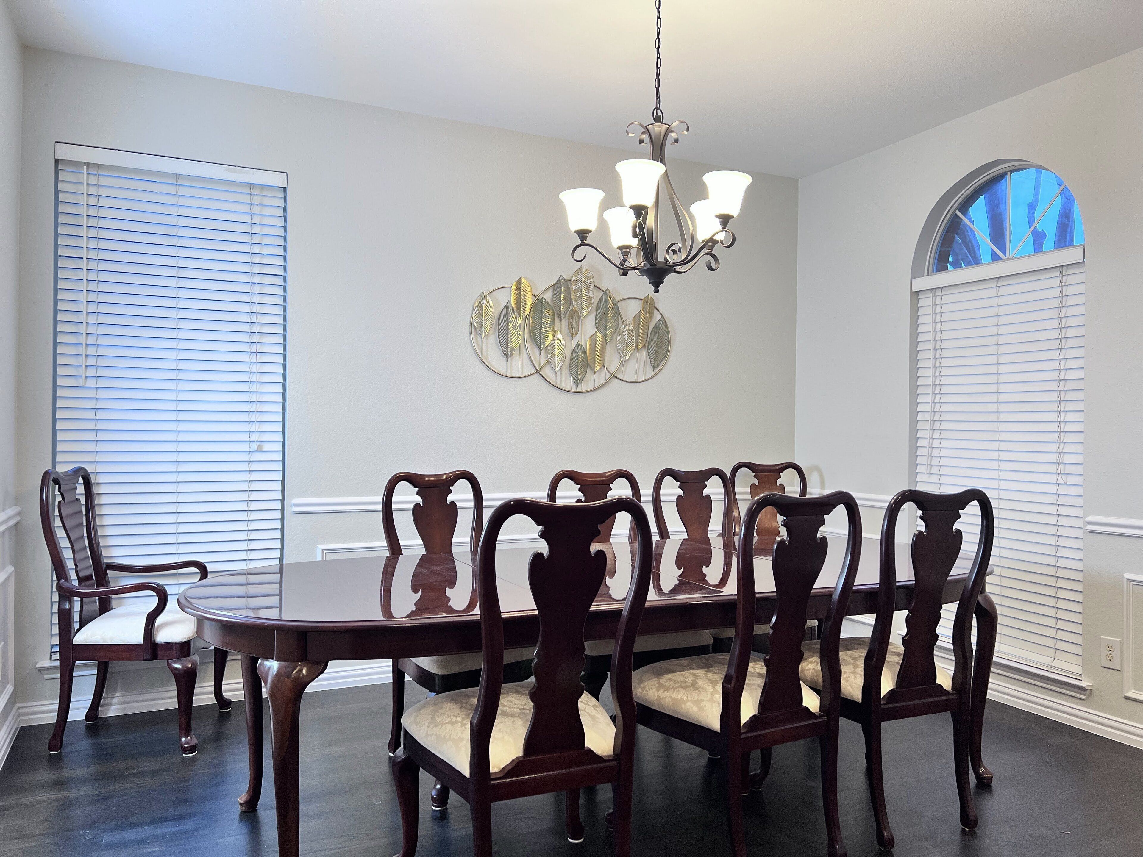 A dining room with a dark wooden table and chairs, a chandelier, and a decorative wall piece.