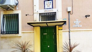 A building with a green door, a yellow awning, and two potted plants. - La casita del Marqués (Alicante)