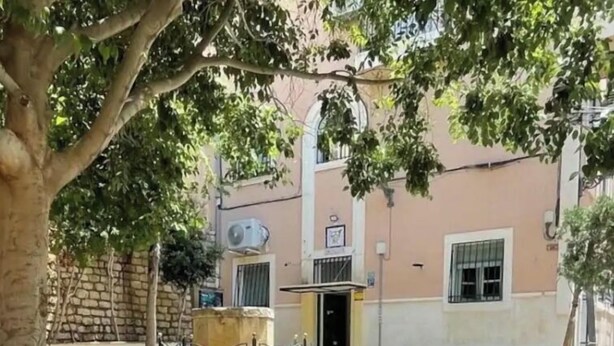 A courtyard with a stone fountain, a bench, and a building with a window and a door. - La casita del Marqués (Alicante)