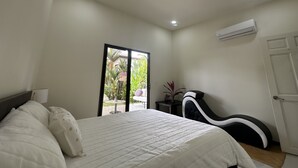 Una camera da letto con un letto, una sedia, un tavolino e una porta vetrata scorrevole che dà su uno spazio esterno.