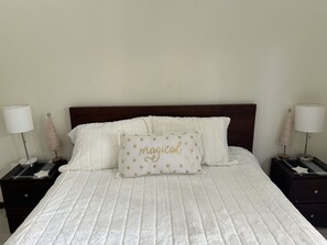 Un letto rifatto con una coperta bianca, un cuscino decorativo con pois dorati e due comodini con lampade e oggetti decorativi.