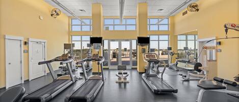 Un gimnasio con cintas de correr, máquinas de pesas y una amplia entrada con ventanas.