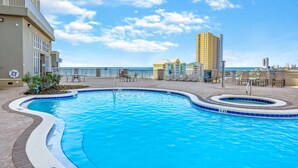 Una piscina de borde curvo, rodeada por una terraza con baldosas y sillas de descanso.