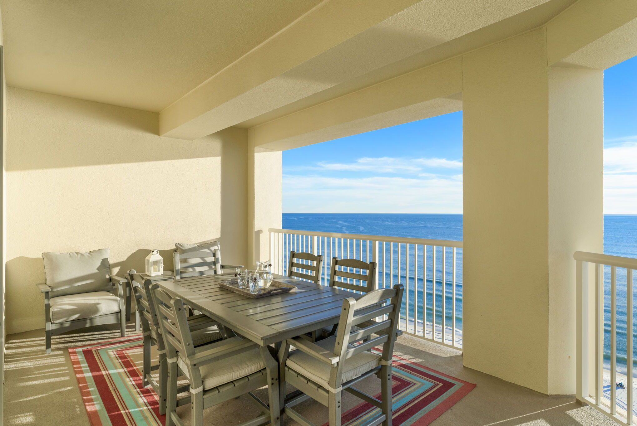 A balcony with a table and chairs, a striped rug, and a view of the ocean.