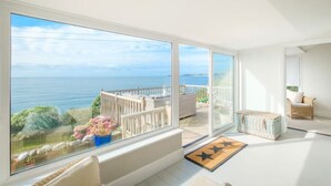 Une pièce lumineuse avec de grandes fenêtres donnant sur une terrasse et la mer.
