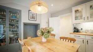 Un coin repas avec une table en bois, des chaises, un vase de fleurs, un luminaire suspendu, et un espace cuisine avec des placards et des appareils électroménagers.