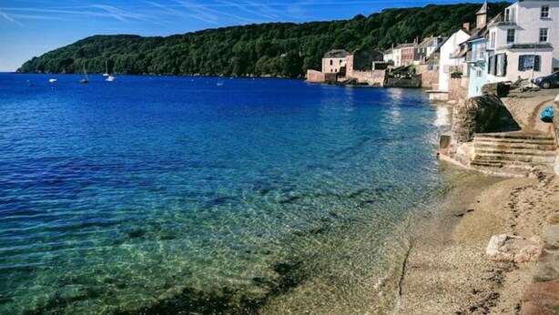 Un paysage côtier avec une eau bleue et limpide, une plage de sable et des bâtiments le long de la côte.