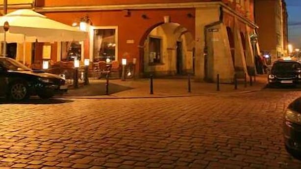 Un bâtiment historique doté d’un toit à forte pente et de nombreuses fenêtres, situé dans une rue pavée, de nuit.