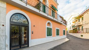 A street view of a building with a large arched window and a door, a balcony with green railings, and a clear sky. - Nisida View Apartment (Pozzuoli)