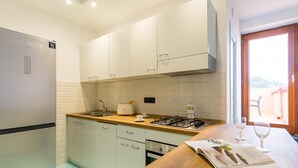 A modern kitchen with white cabinets, a stainless steel refrigerator, a wooden countertop, a gas stove, and a window with a view of the outdoors. - Nisida View Apartment (Pozzuoli)