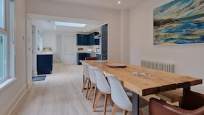 Et moderne spiseområde med et langt træbord, hvide stole og en læderstol i brunt.